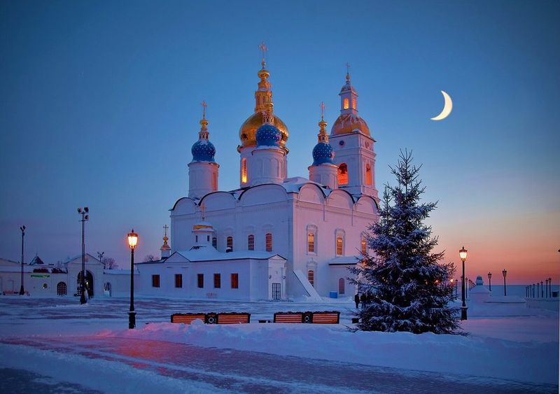 A blue and white cathedral in deep snow beneath a crescent moon at dawn.